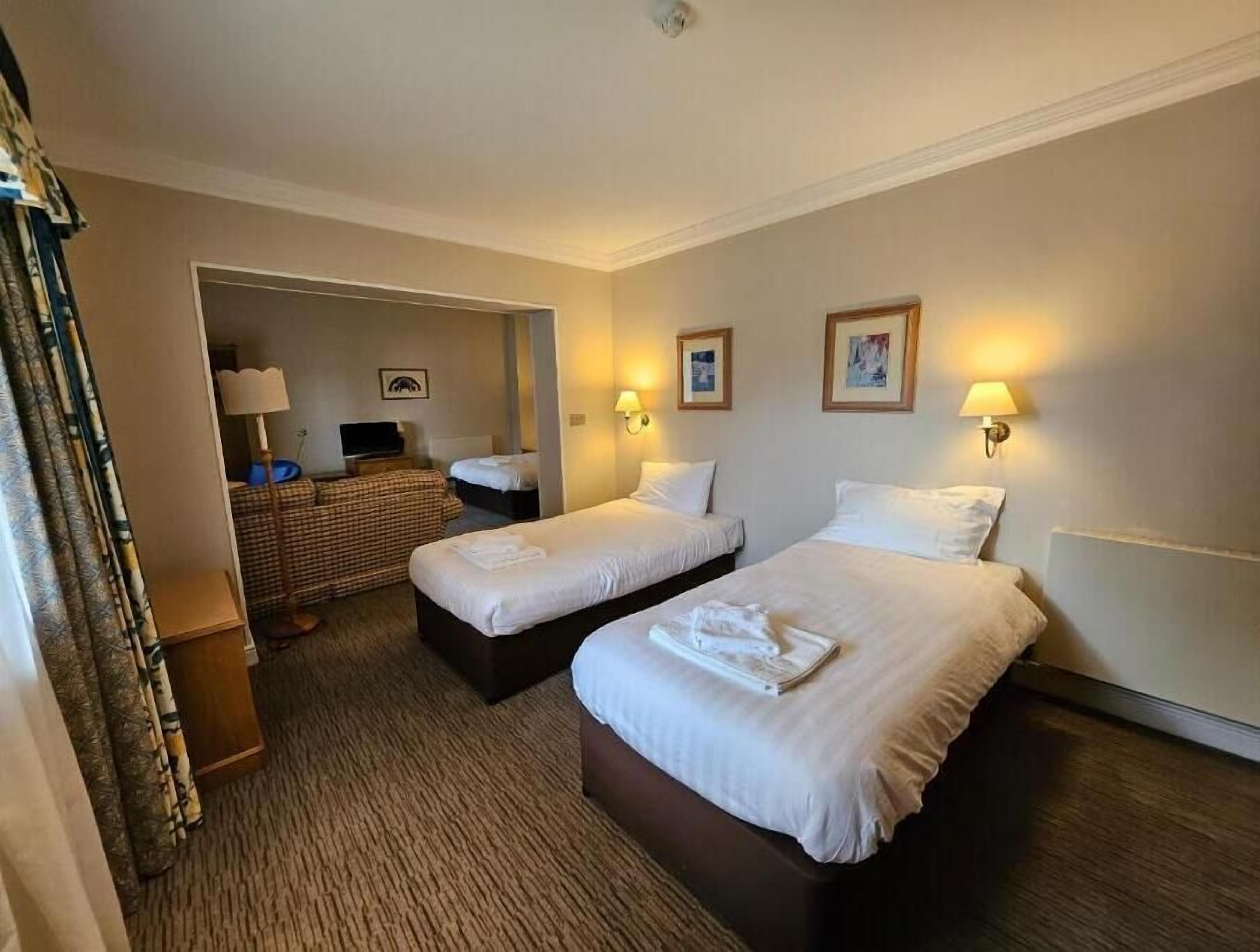 A hotel room with two beds, a desk, a chair, a mirror, and two wall-mounted lamps.