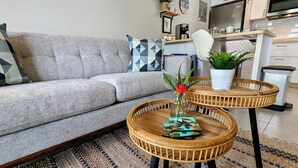 Ein modernes Wohnzimmer mit einem grauen Sofa, zwei runden Holztischen, einer Topfpflanze und einer Kaffeemaschine.