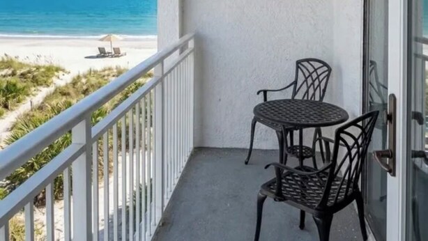 Ein Balkon mit Tisch und Stühlen mit Blick auf Strand und Meer.