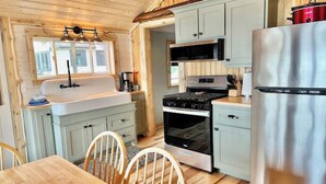 A compact kitchen with a sink, stove, refrigerator, and wooden cabinets. - Cabin on the beach with lakeviews and fireplace (AU TRAIN)