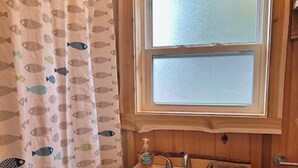 A bathroom with a white sink, a window above it, and a shower curtain with fish patterns. - Cabin on the beach with lakeviews and fireplace (AU TRAIN)