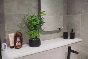 A bathroom with a white countertop, a bamboo plant, a bottle of lotion, and a black faucet. - Cosy Modern 1BR in East Parade Sheffield (Sheffield)