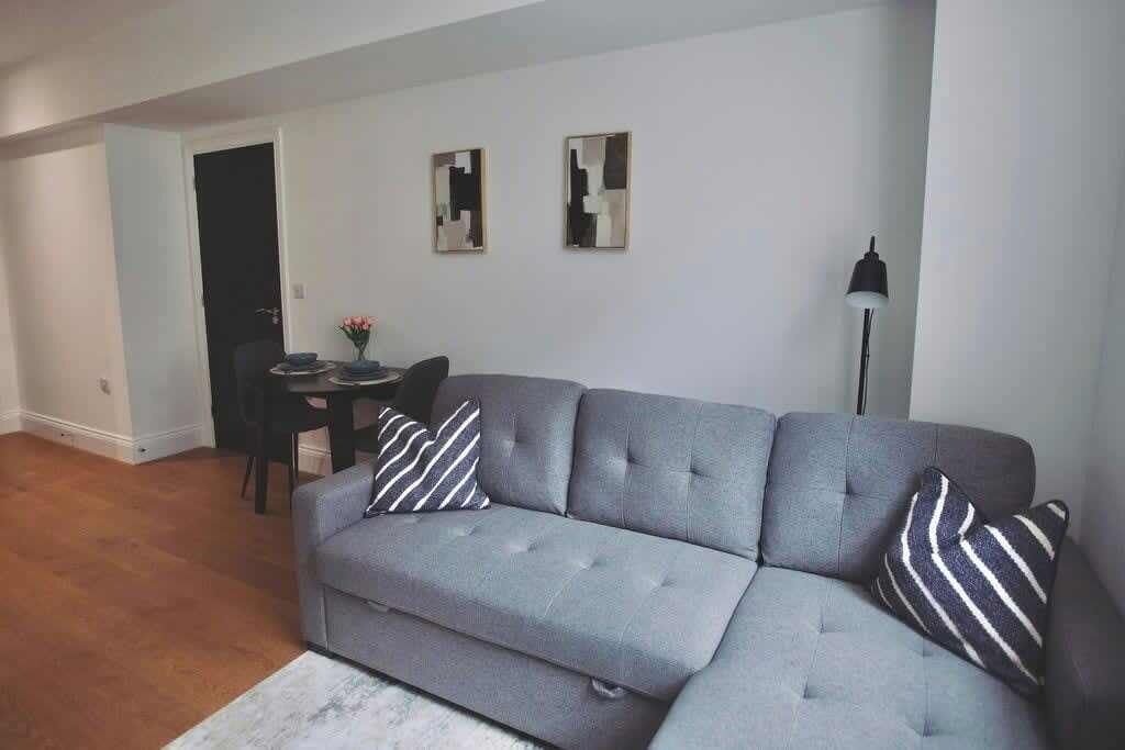 En stue med en grå sofa, to sofaborde, en lænestol og en lampe.