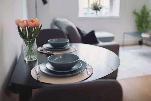 A dining table set with plates, bowls, and cutlery, accompanied by a vase of flowers. - Cosy Modern 1BR in East Parade Sheffield (Sheffield)