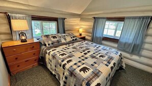 Quarto com cama, cómoda de madeira, duas luminárias de cabeceira e janela com cortinas.