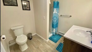 Ein Badezimmer mit Toilette, Mülleimer, einer Dusche mit blau gemustertem Vorhang und Waschbecken mit Spiegel.