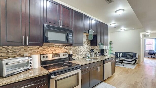 A modern kitchen with dark wood cabinets, a built-in microwave, a stove, and a toaster. - Spacious 5-bedroom apartment in lovely Philadelphia with WiFi, Free Parking (Philadelphia)