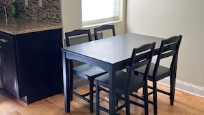 A kitchen with a dark countertop, a window with blinds, and a dining table with four chairs. - Spacious 5-bedroom apartment in lovely Philadelphia with WiFi, Free Parking (Philadelphia)