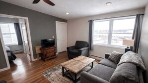 Ein Wohnzimmer mit Sofa, Couchtisch, Fernseher auf einer Holzkommode und Blick durch ein großes Fenster.