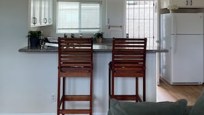 A kitchen with a central island, two wooden bar stools, a white refrigerator, and a window with blinds. - Cozy 2Bed-Private Parking, Dog Friendly, Big Yard! (San Diego)
