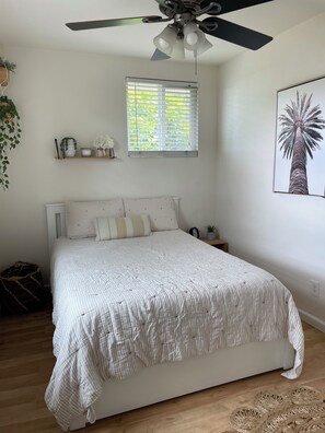 A bedroom with a bed, a ceiling fan, a window with blinds, a wall-mounted shelf with decorative items, and a framed picture. - Cozy 2Bed-Private Parking, Dog Friendly, Big Yard! (San Diego)