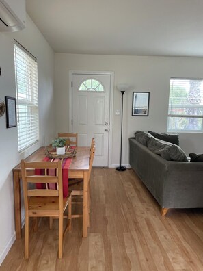A dining area with a wooden table and chairs, a white door, and a grey sofa. - Cozy 2Bed-Private Parking, Dog Friendly, Big Yard! (San Diego)