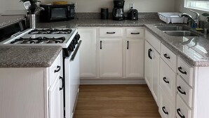 A kitchen with white cabinets, a gas stove, a coffee maker, and a sink. - Cozy 2Bed-Private Parking, Dog Friendly, Big Yard! (San Diego)