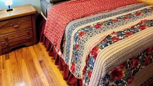 A wooden-paneled room with a bed, a nightstand, a window with blinds, and a lamp.