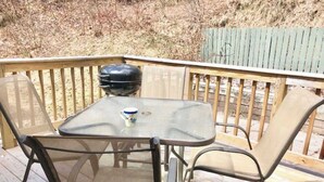 A deck with a table and chairs, a grill, and a wooden fence in the background.