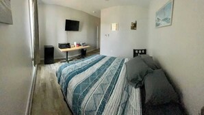 A bedroom with a bed, a desk, a chair, a TV, and a window. - Upstairs Suite at the entrance to Pictured Rocks (Munising)
