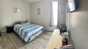 A bedroom with a bed, a desk, a chair, a TV, and a window. - Upstairs Suite at the entrance to Pictured Rocks (Munising)