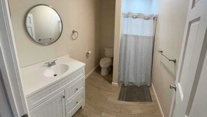 A bathroom with a sink, mirror, toilet, and shower curtain. - Upstairs Suite at the entrance to Pictured Rocks (Munising)