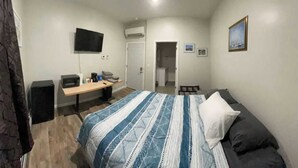 A bedroom with a bed, a desk, a chair, a TV, and an air conditioning unit.