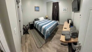 A bedroom with a bed, a desk, a chair, a TV, and a door.