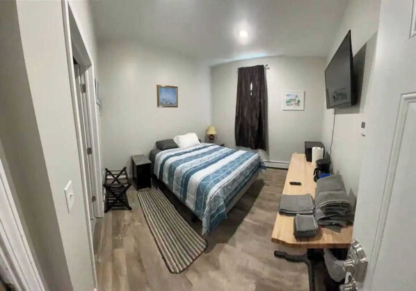 Ein Schlafzimmer mit Bett, Schreibtisch, Stuhl, Fernseher und einer Tür.