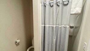A bathroom with a shower curtain, toilet, and wooden flooring.