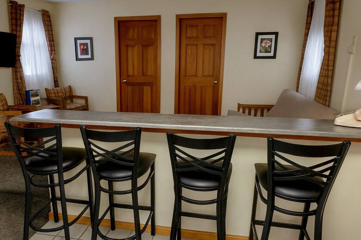 Una cocina con barra, tres taburetes negros, dos puertas de madera y suelo de baldosas.