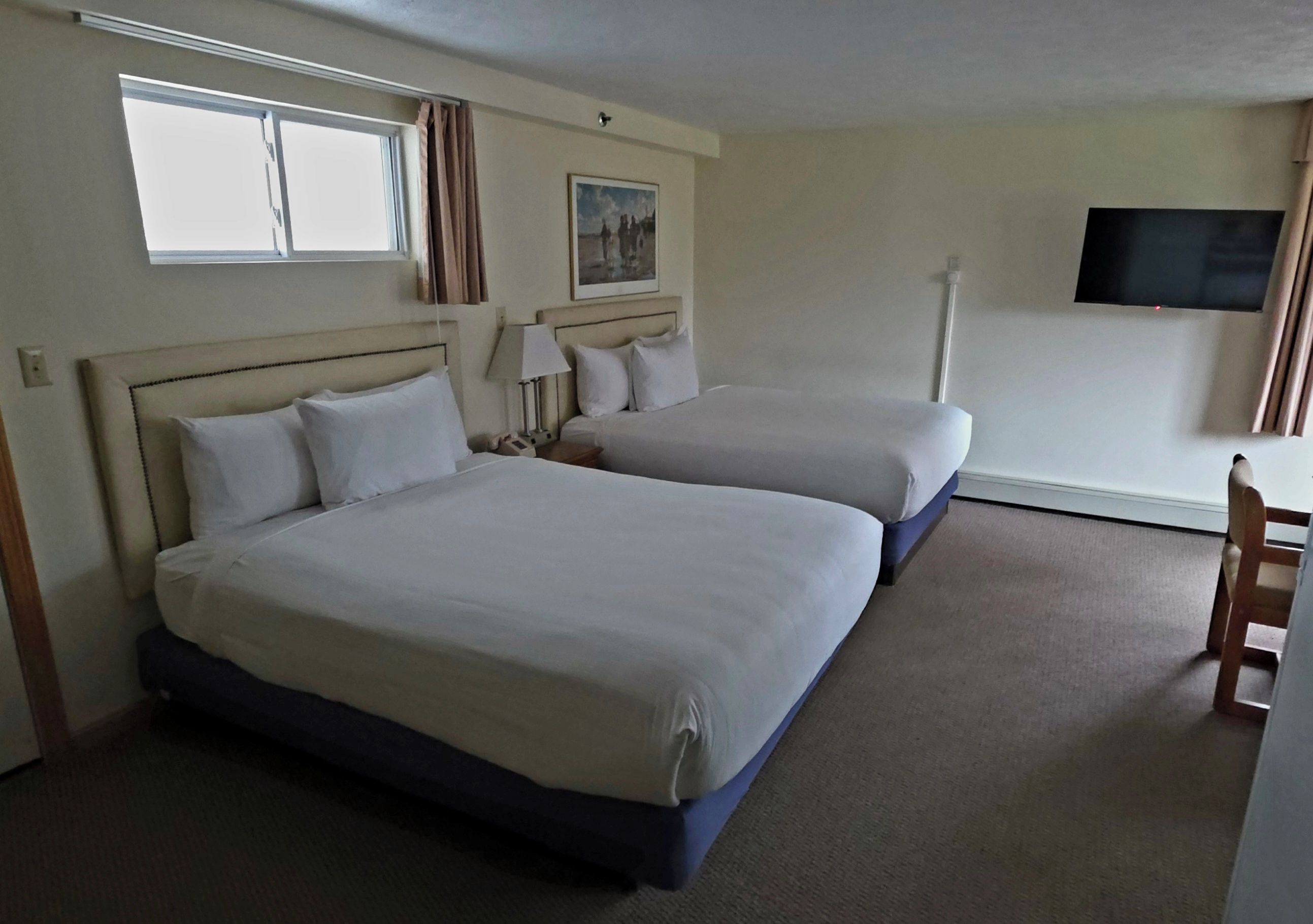 A hotel room with two beds, a TV, a window, and a chair.