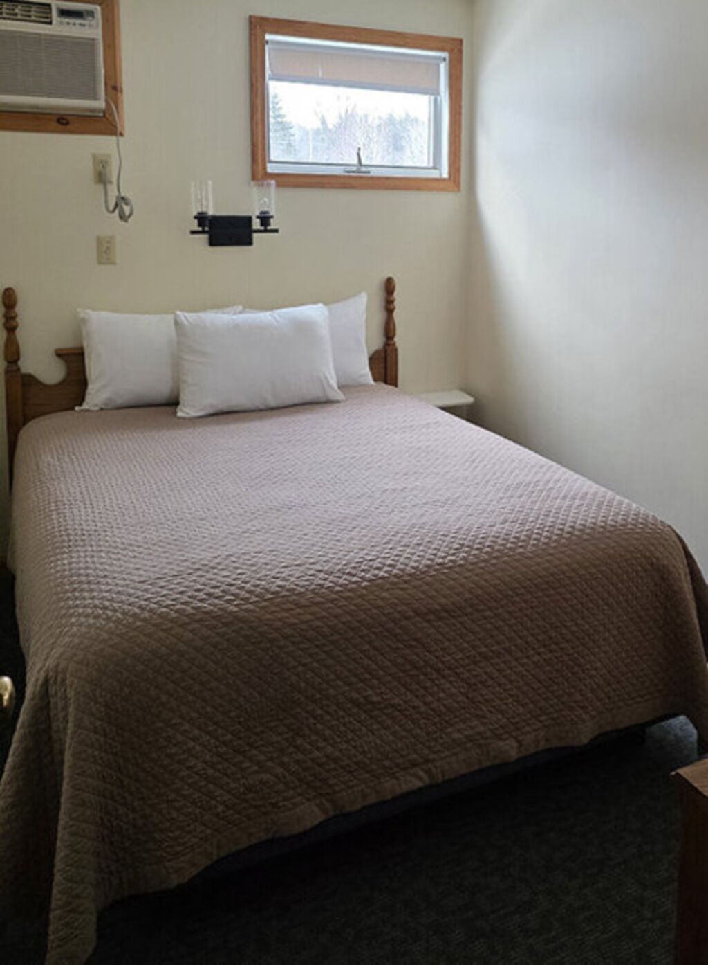 A bedroom with a bed, a window, an air conditioning unit, and a nightstand.