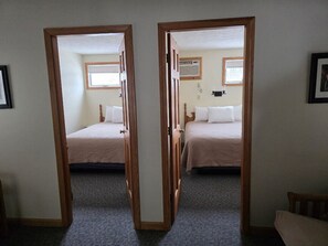 A room with two beds, a wooden door frame, and a carpeted floor.