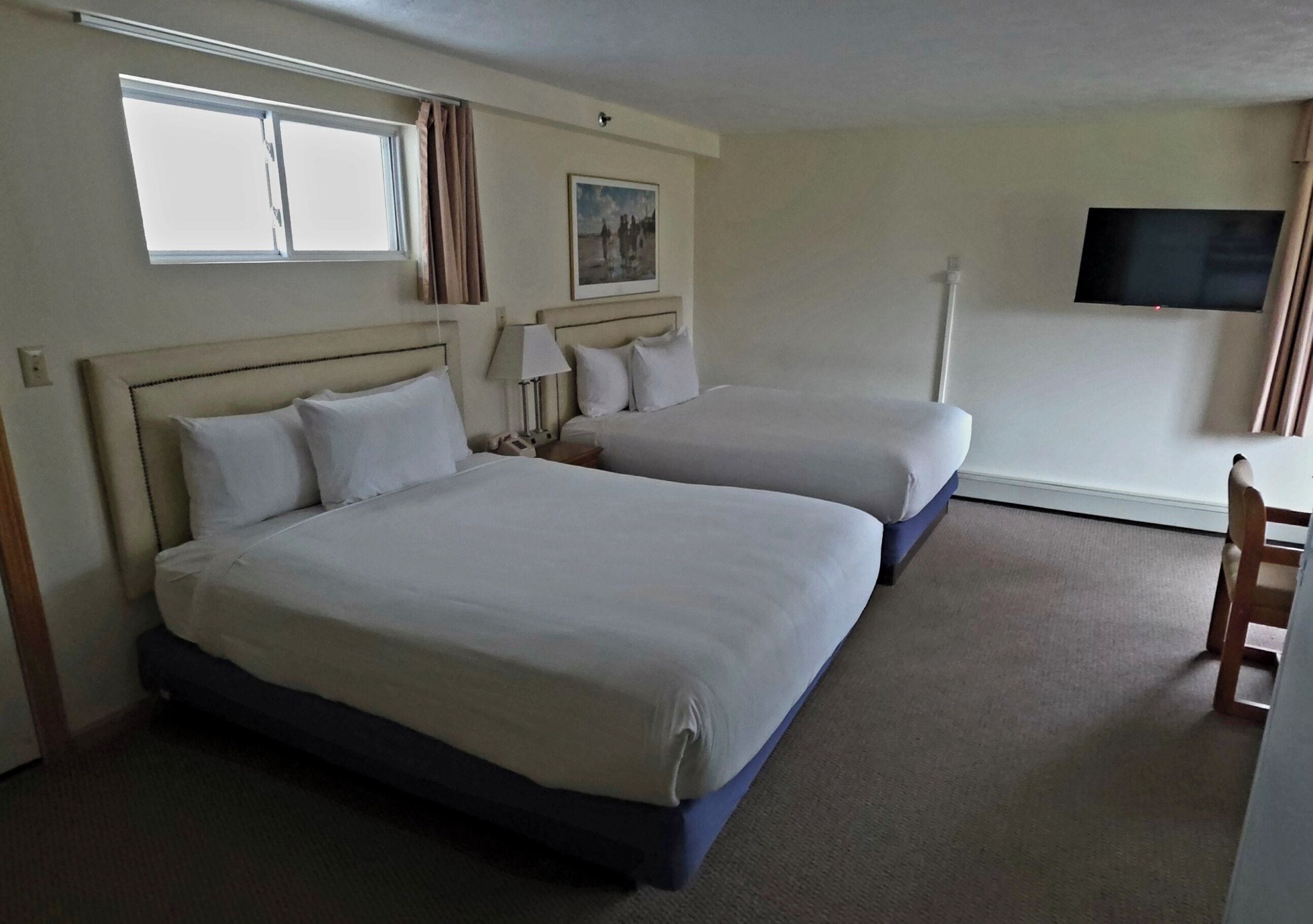 A hotel room with two beds, a TV, a window, and a chair.