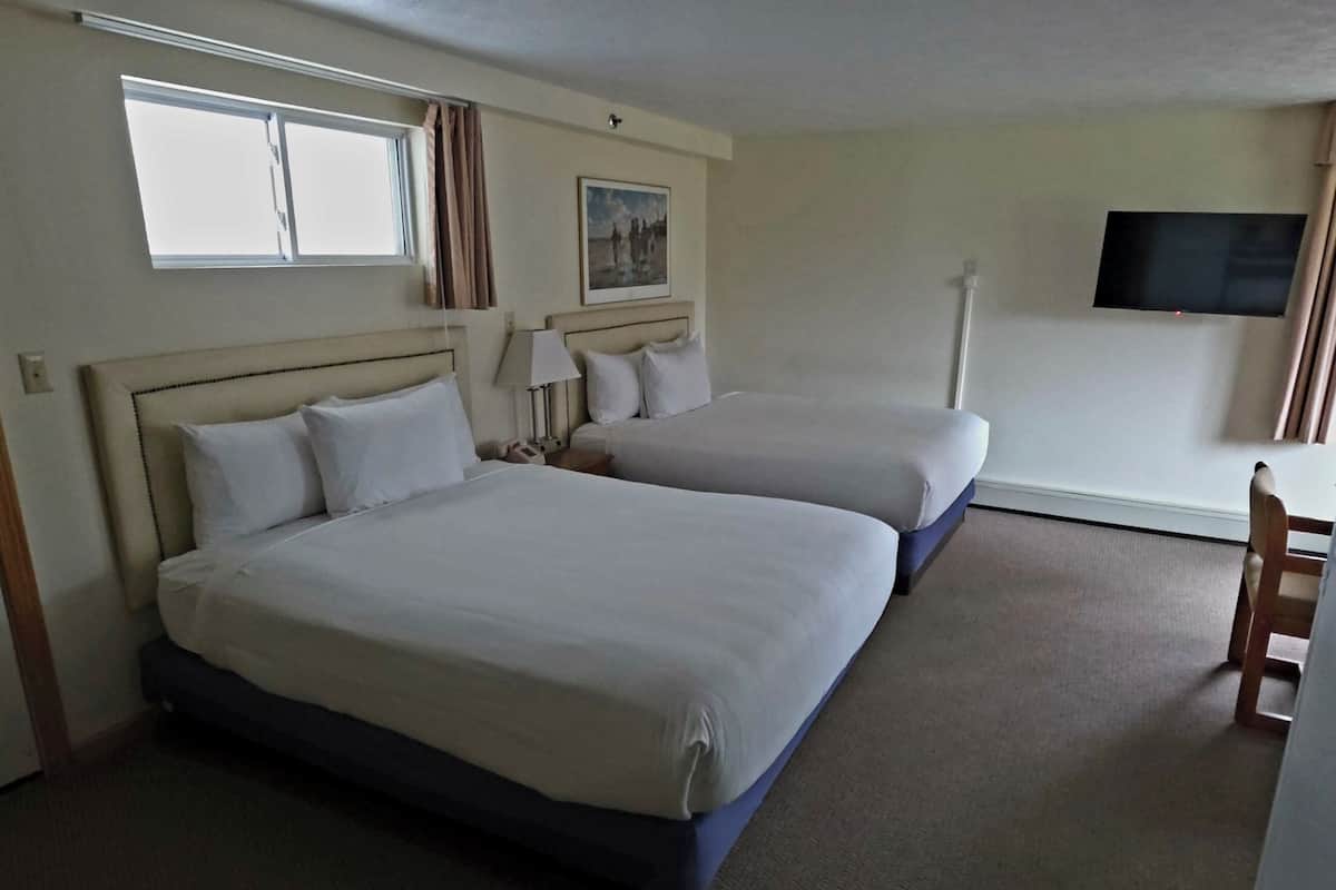 A hotel room with two beds, a TV, a window, and a chair.