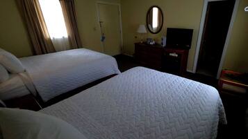 A hotel room with two beds, a dresser, a mirror, a television, and a door.