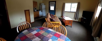 Una habitación con mesa de comedor, sillas, una pequeña cocina y televisor.