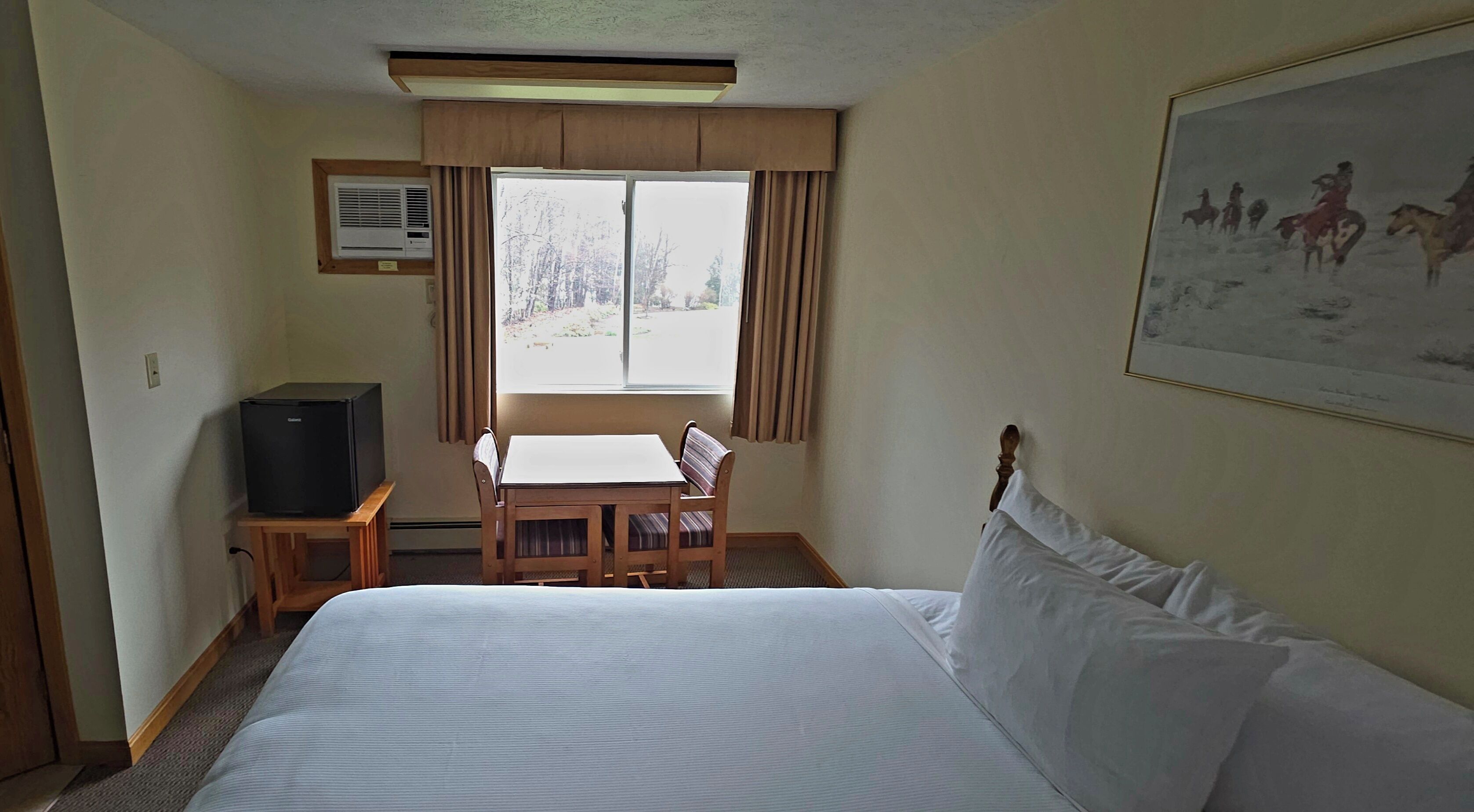 Ett hotellrum med en säng, ett skrivbord med en stol, en tv och ett fönster med gardiner.
