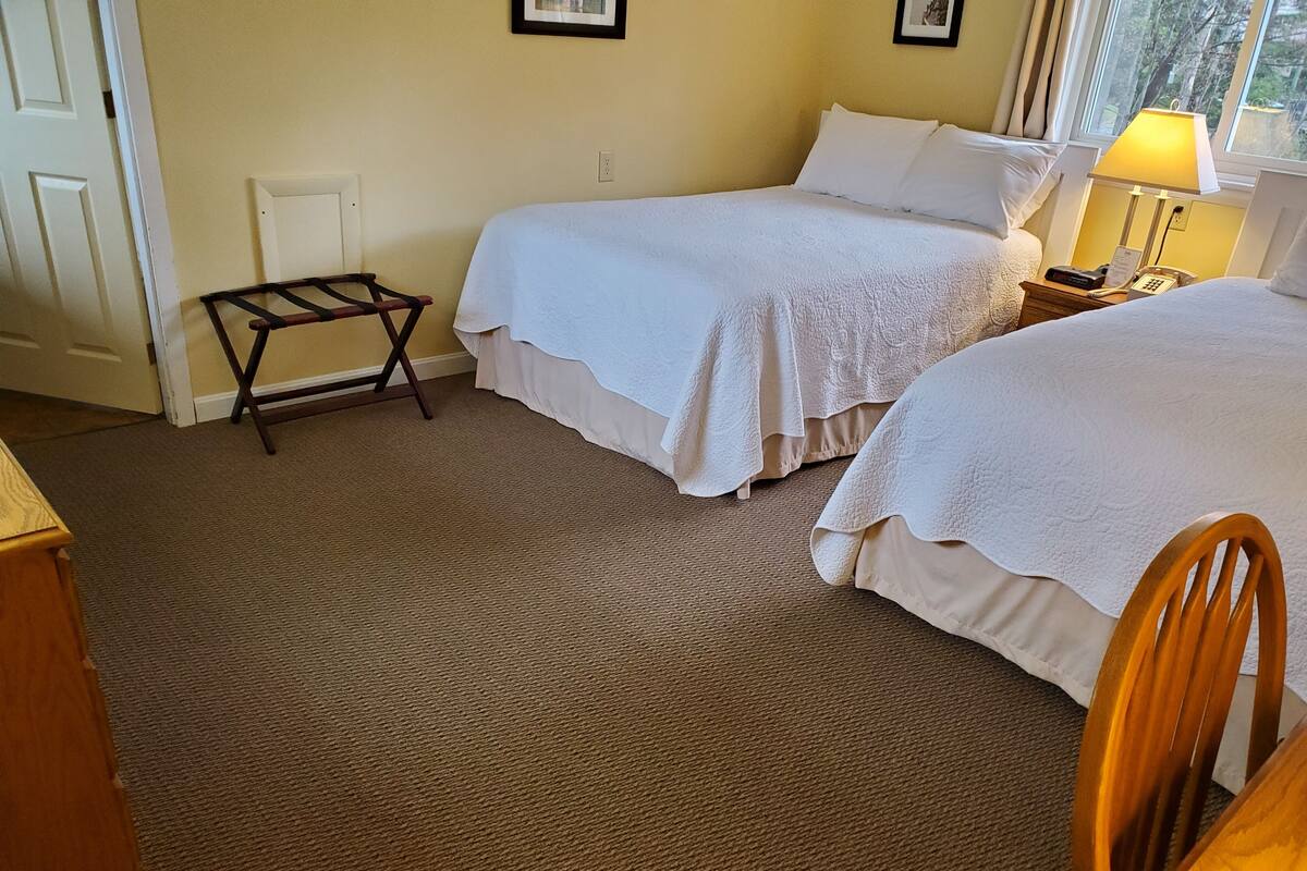Habitación de hotel con dos camas, una mesita, una silla y una ventana con vistas.