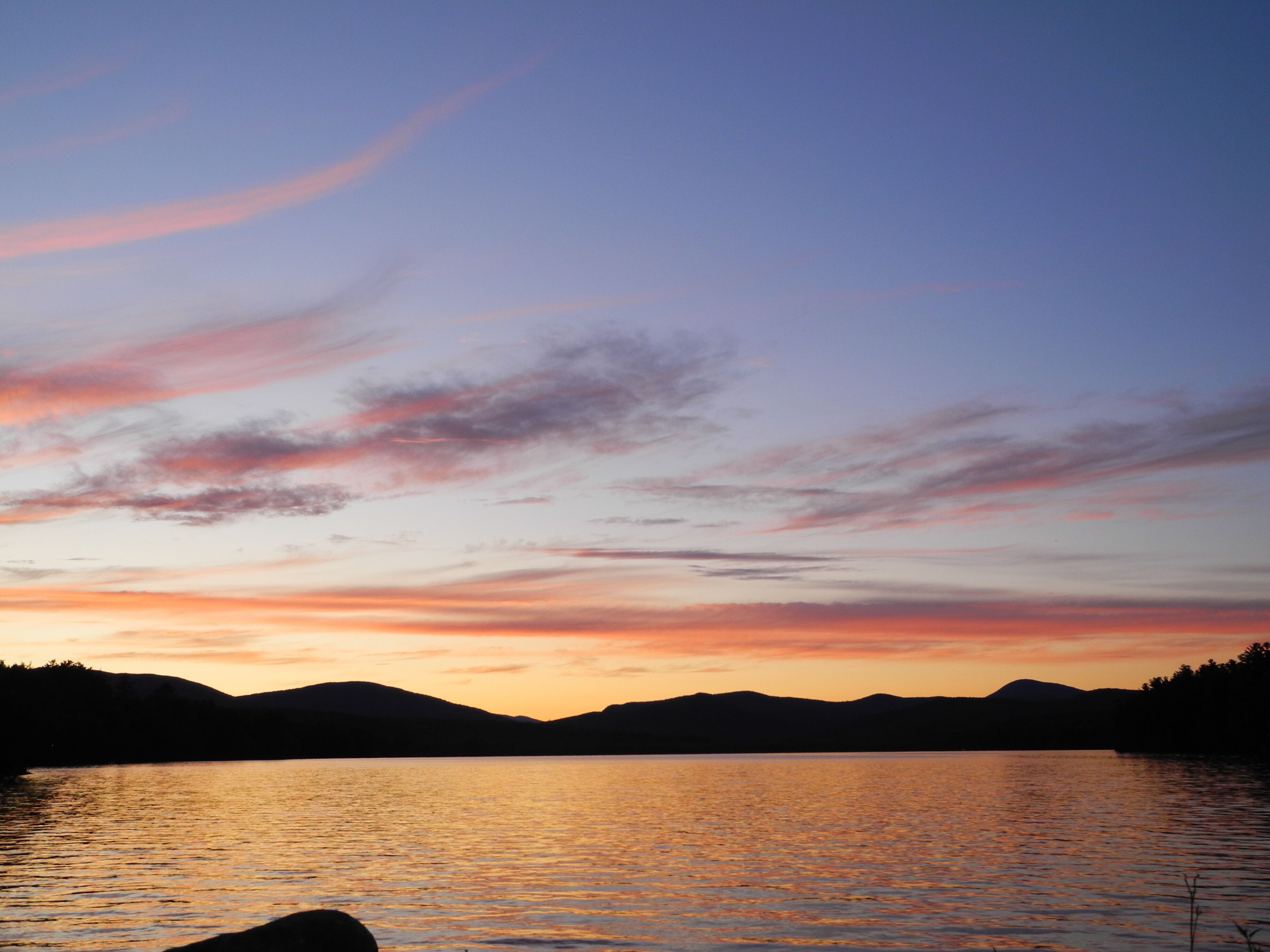 A sunset over a calm lake with distant mountains.