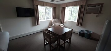 Una habitación con una mesa y sillas de madera, un televisor de pantalla plana montado en la pared y una ventana con cortinas.
