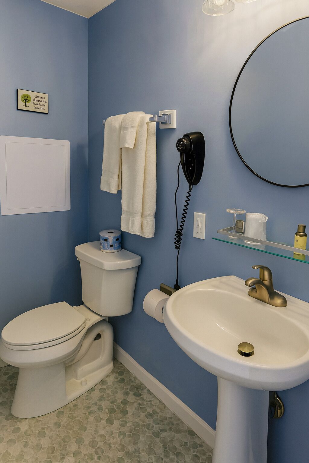 Un baño con inodoro, lavamanos y secador de pelo fijado a la pared.