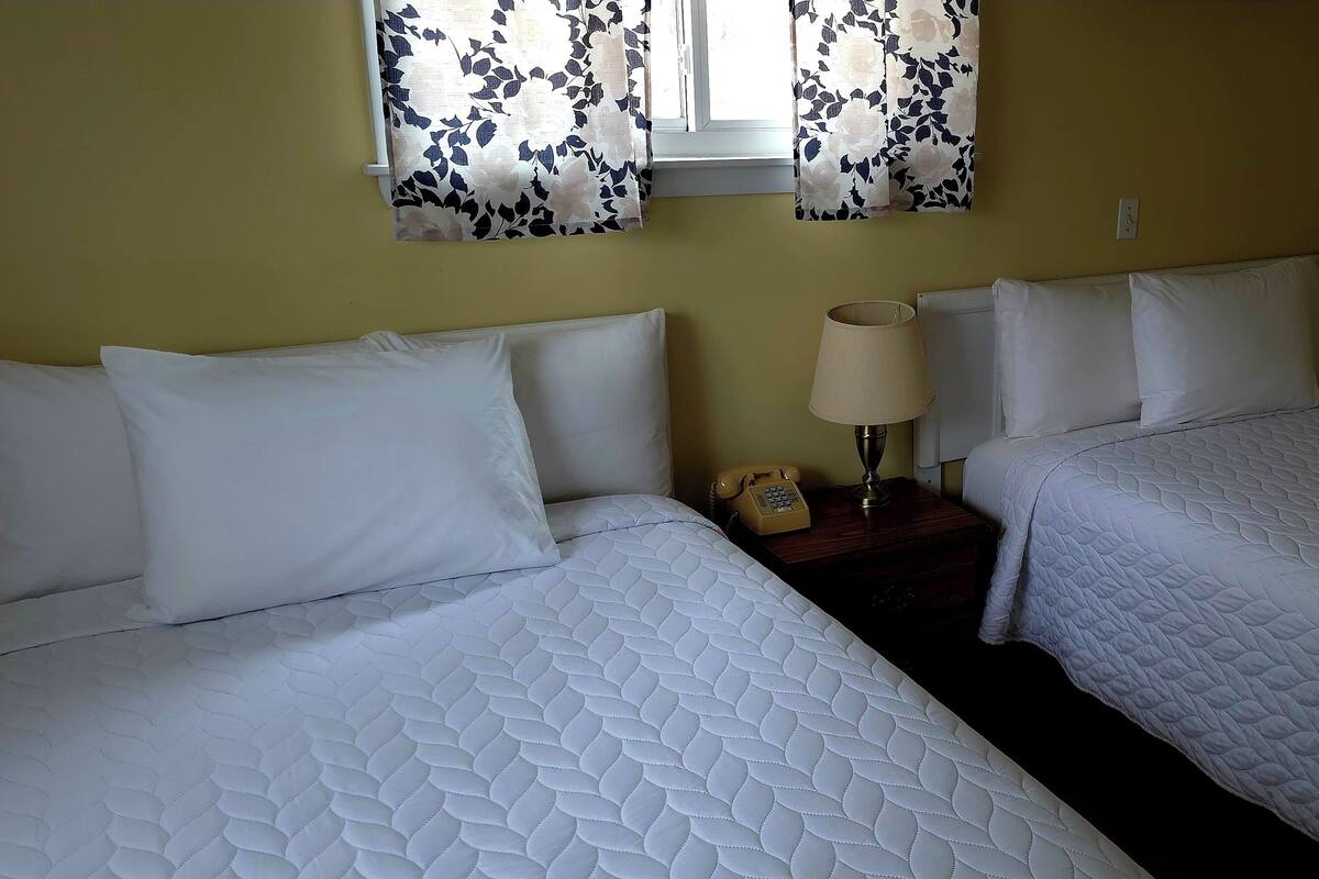 Habitación doble con dos camas, una mesita de noche con lámpara y teléfono.
