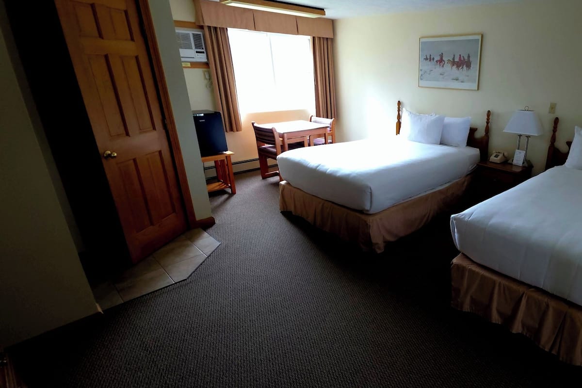 A hotel room with two beds, a desk, a chair, a lamp, and two paintings on the walls.