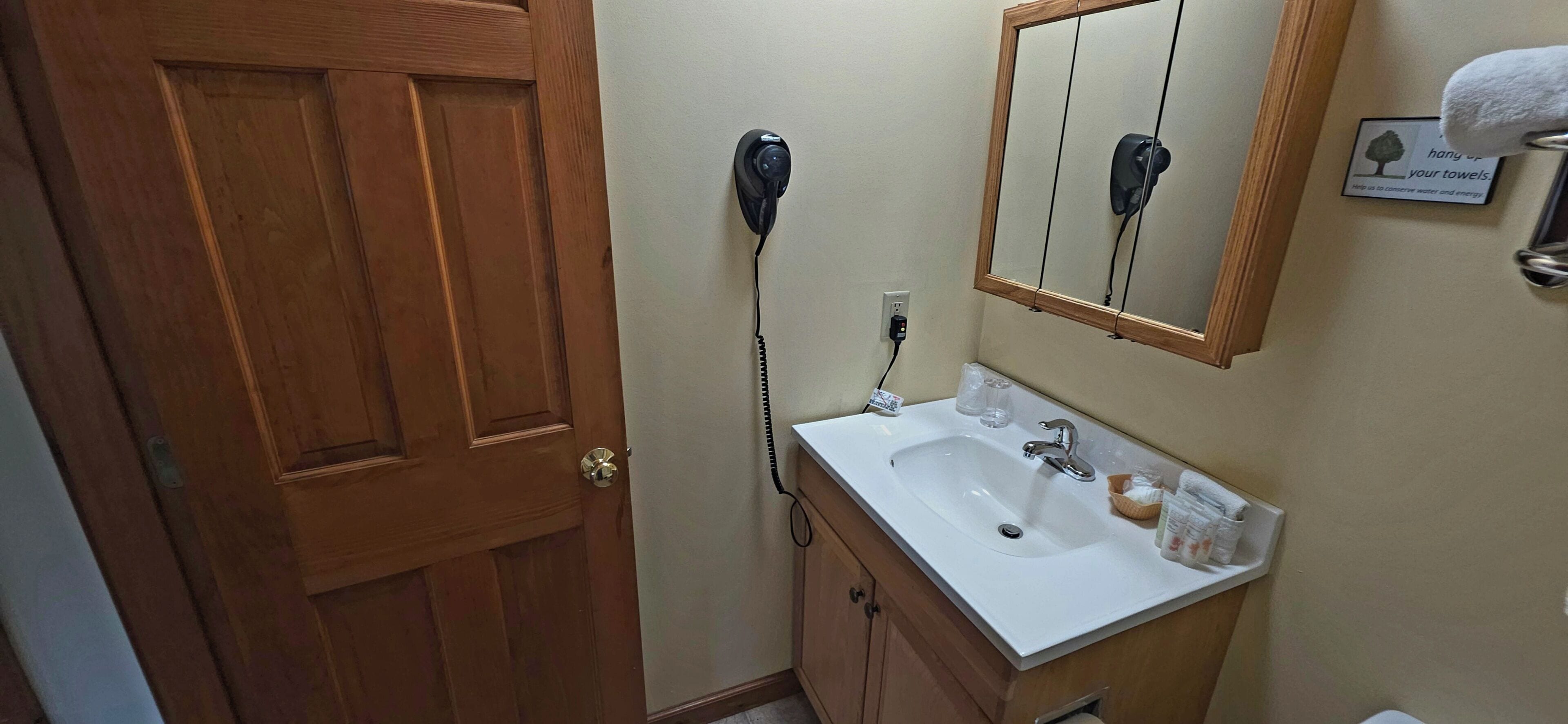 A wooden door, a white sink with a mirror above it, and a towel rack with a towel.