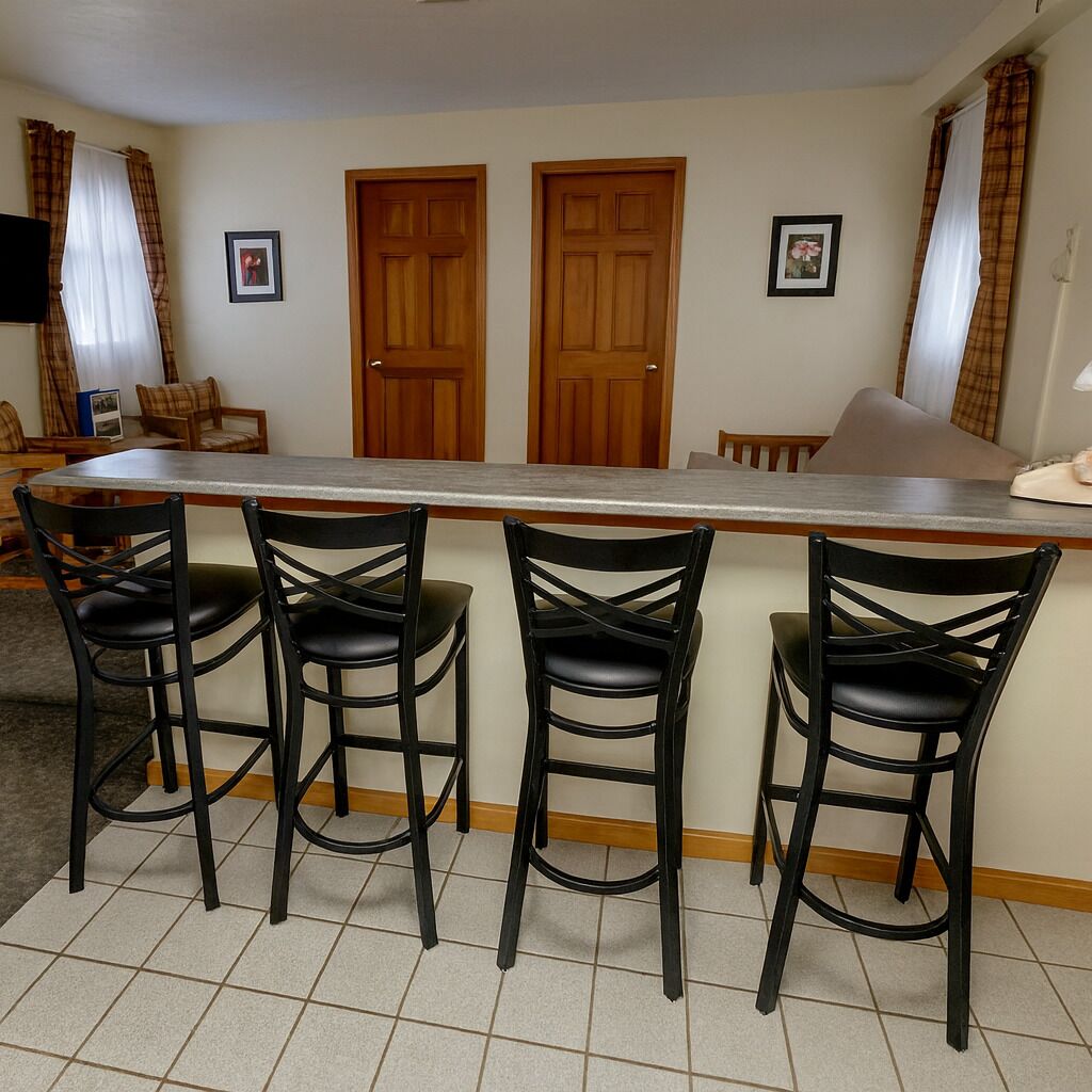 A kitchen with a bar area, three black bar stools, two wooden doors, and a tiled floor.