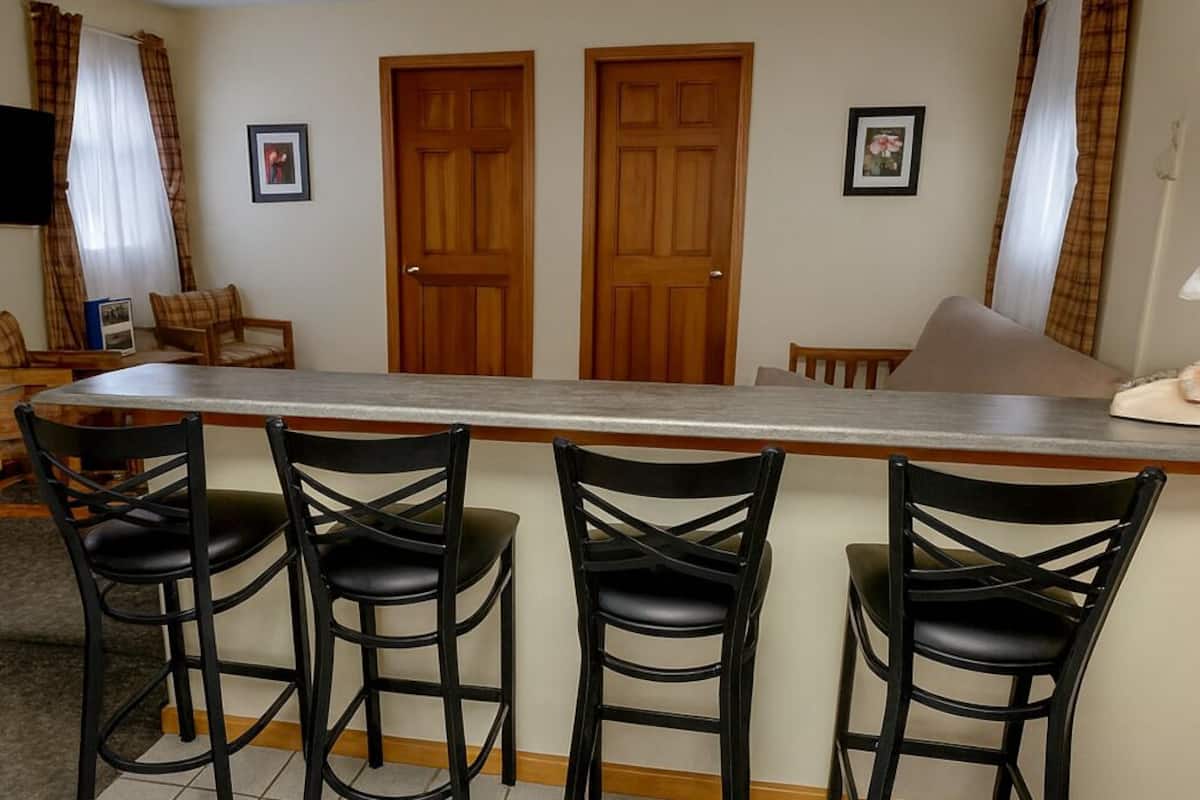 A kitchen with a bar area, three black bar stools, two wooden doors, and a tiled floor.