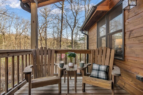 A wooden deck with a table and chairs, a potted plant, and a window overlooking a forest. - New Listing! Family Gameroom Cabin+Fire Pit+Hot Tub+Dog Friendly+Close to BR! (Morganton)