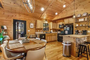 A wooden cabin interior with a dining area, kitchen, and a small bar area. - New Listing! Family Gameroom Cabin+Fire Pit+Hot Tub+Dog Friendly+Close to BR! (Morganton)