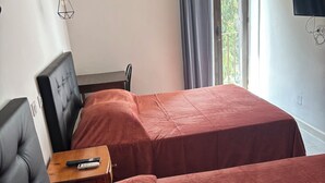 A hotel room with two beds, a small table with a remote control, a black leather chair, a window with curtains, and a wall-mounted TV. - Hotel beautiful stay in porto-ota 105 (Ota)