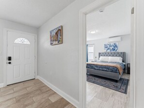 A bedroom with a bed, a nightstand, a wall-mounted light, and a door. - Clearwater First Floor #1 (Clearwater)