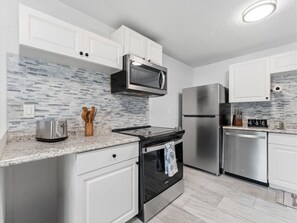 A modern kitchen with white cabinets, a microwave, a toaster, a stove, a refrigerator, and a dishwasher. - Clearwater First Floor #1 (Clearwater)