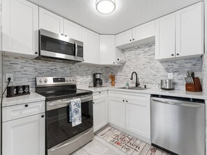 Una cocina moderna con gabinetes blancos, un microondas de acero inoxidable, una cafetera y un lavavajillas.